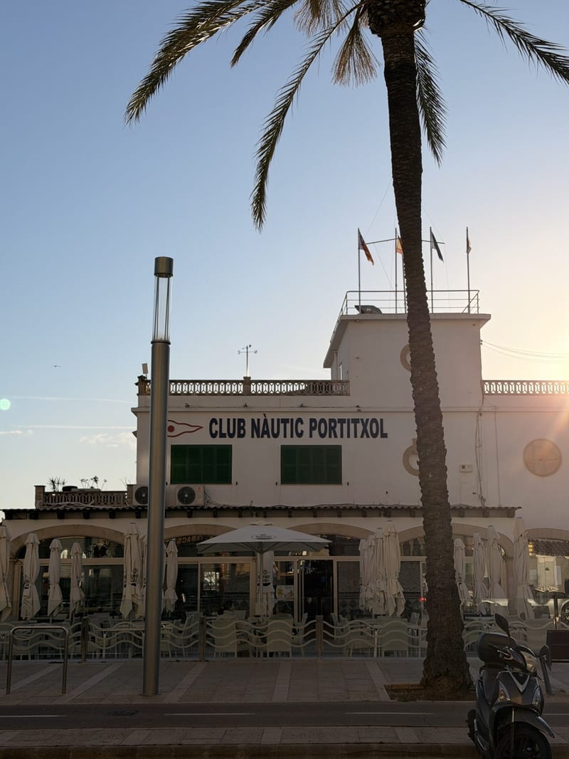 Gebäude des Club Nàutic Portitxol mit Terrasse und Palme im Abendlicht