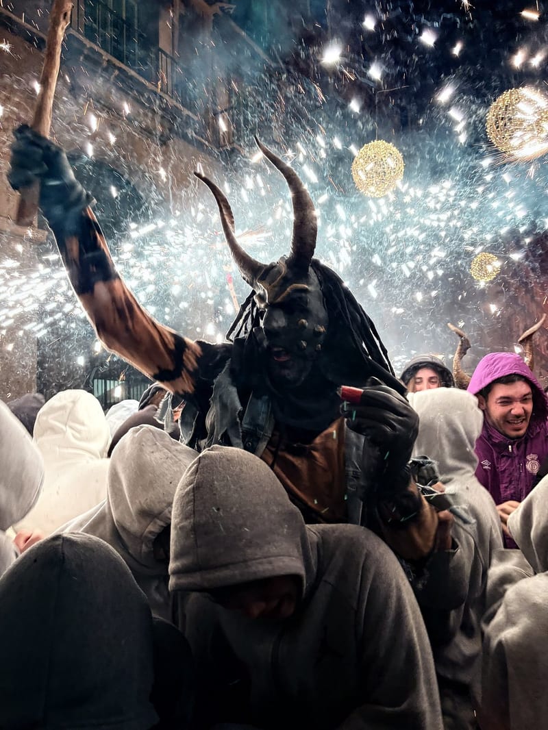 Als Teufel verkleidete Figur mit Hörnern zwischen sprühenden Funken bei einem Correfoc in Palma, umringt von Menschen mit Kapuzen
