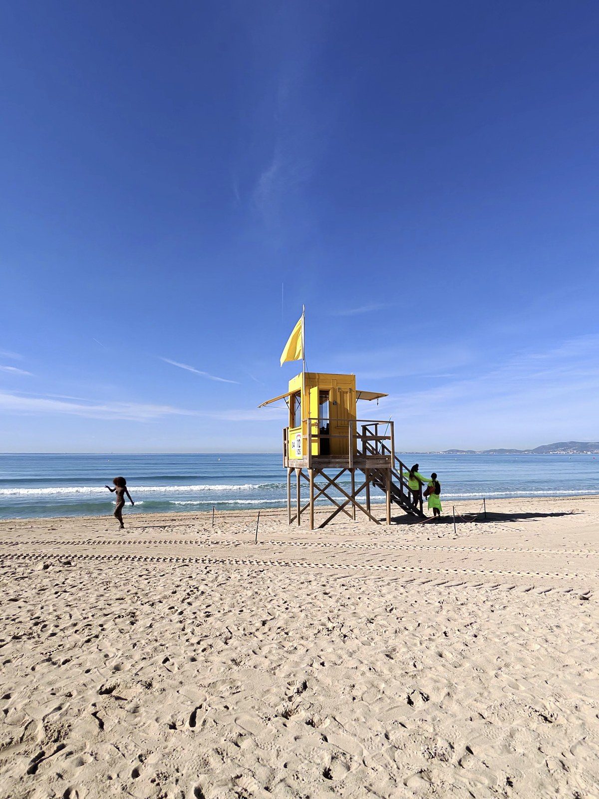 Gelber Rettungsschwimmer-Turm mit gelber Flagge am Strand der Playa de Palma unter blauem Himmel