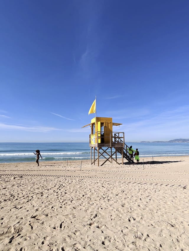Gelber Rettungsschwimmer-Turm mit gelber Flagge am Strand der Playa de Palma unter blauem Himmel