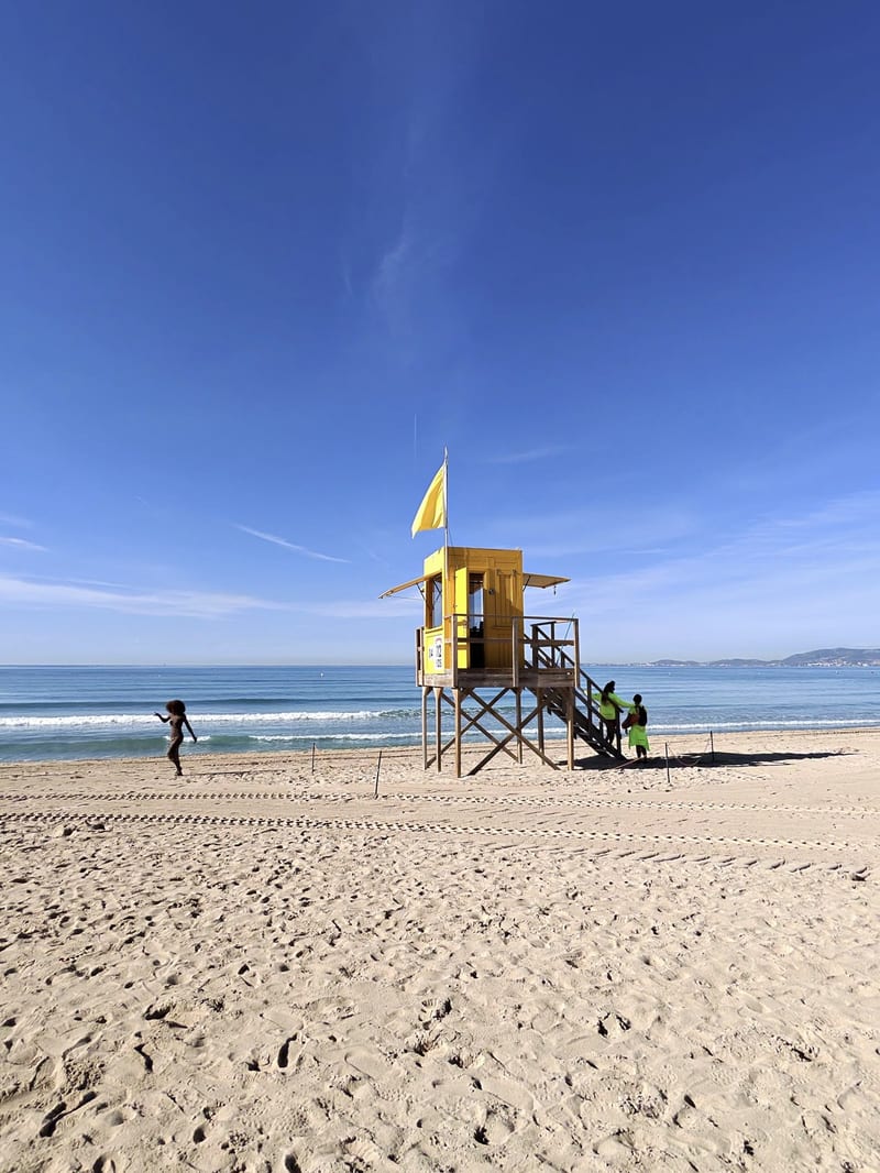 Gelber Rettungsschwimmer-Turm mit gelber Flagge am Strand der Playa de Palma unter blauem Himmel