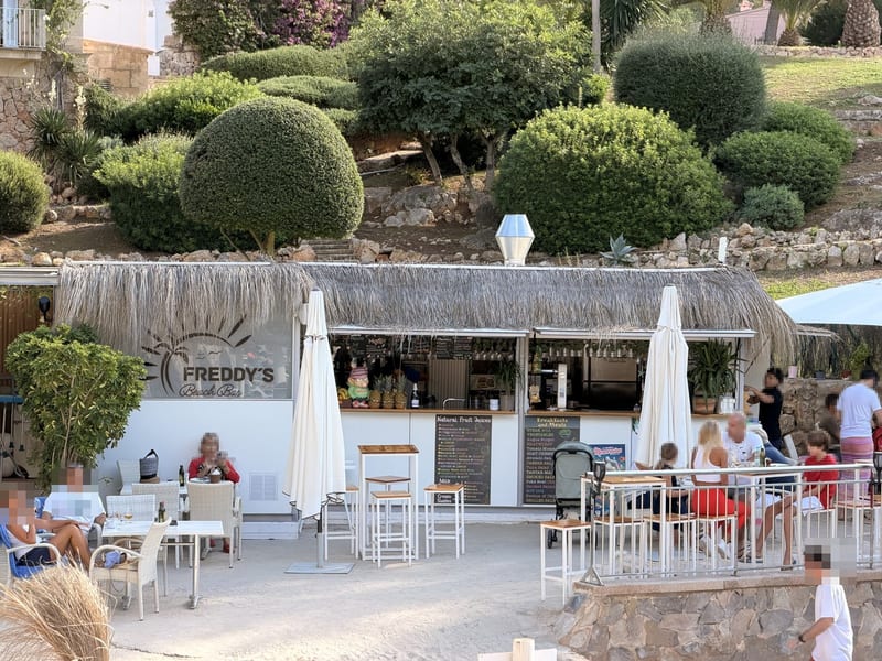 Die Bar von Freddy’s Beach Bar & Restaurant mit Reetdach und Schild, Gäste an Tischen