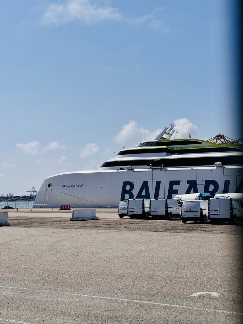 Weiße Baleària-Schnellfähre „Margarita Salas“ am Kai im Hafen, davor mehrere weiße Transporter auf dem Hafengelände, blauer Himmel