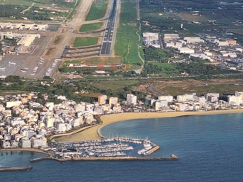 Luftbild des Flughafens Palma de Mallorca mit Start- und Landebahn, dahinter Can Pastilla mit Strand und Yachthafen