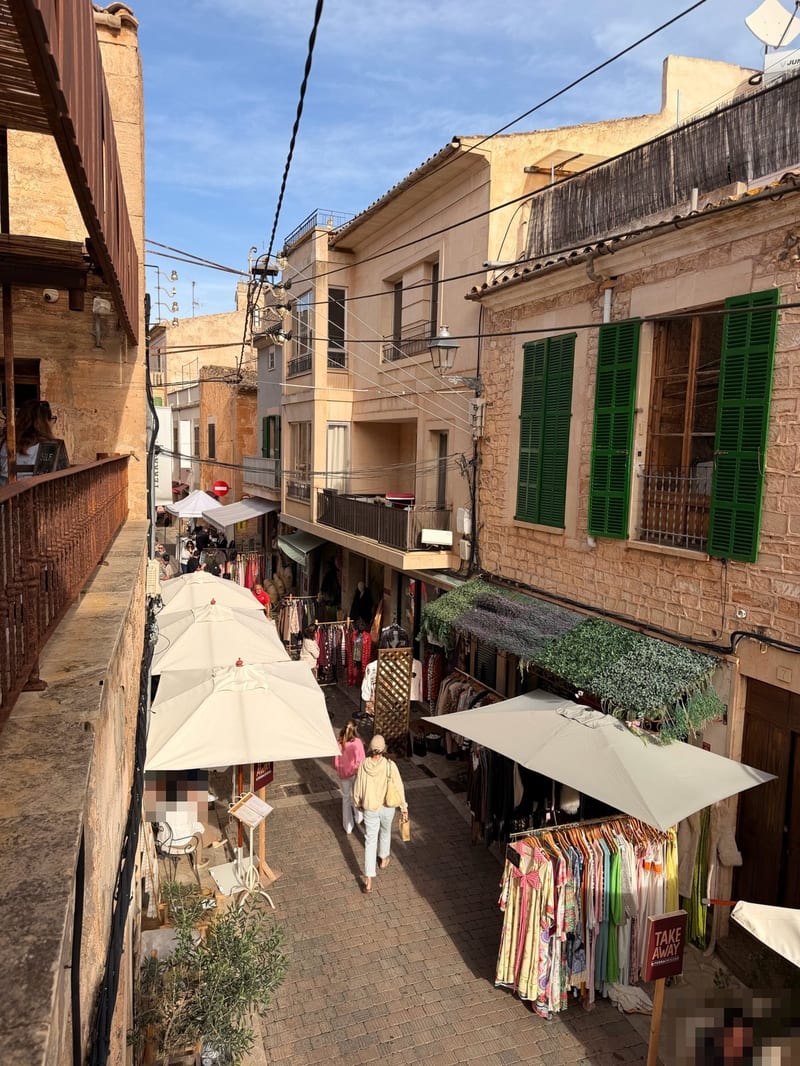 Blick von oben in eine schmale Gasse mit Sonnenschirmen und Kleiderständern, grüne Fensterläden