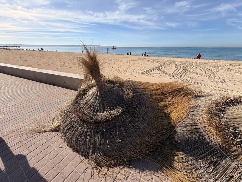 Zusammengeklappte Reetschirme und Liegen auf dem Strandweg der Playa de Palma, dahinter Sand und Meer