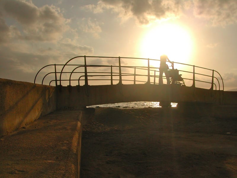 Kleine Fußgängerbrücke an der Promenade von Es Molinar im Gegenlicht der Sonne